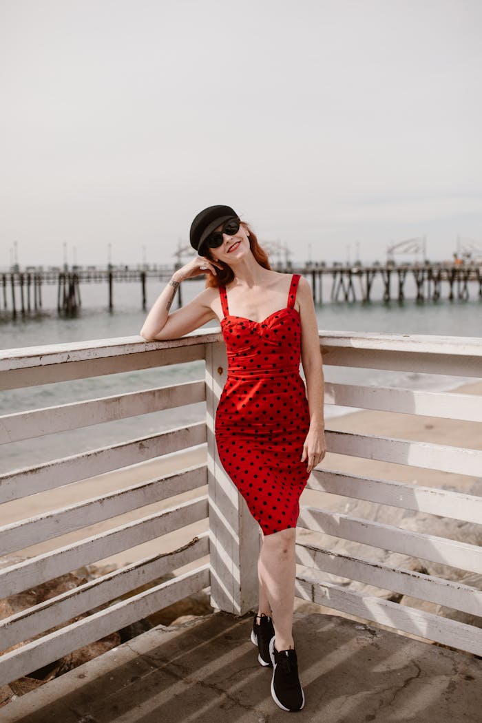 The Art of Drawing Readers In: Your attractive post title goes here Elegant woman in a red polka dot dress enjoys a sunny day at the beach pier, showcasing vibrant summer fashion.